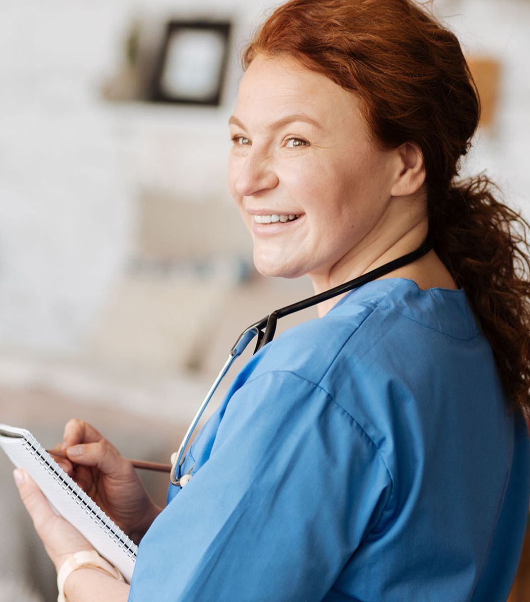 Nurse holding clipboard and smiling, looking off camera.