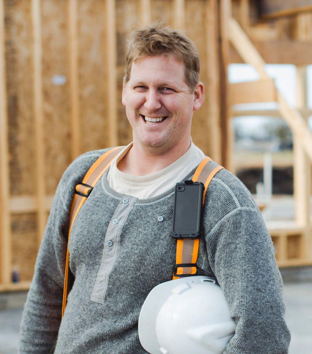 Man wearing heavy duty suspenders holding a white hard hat.