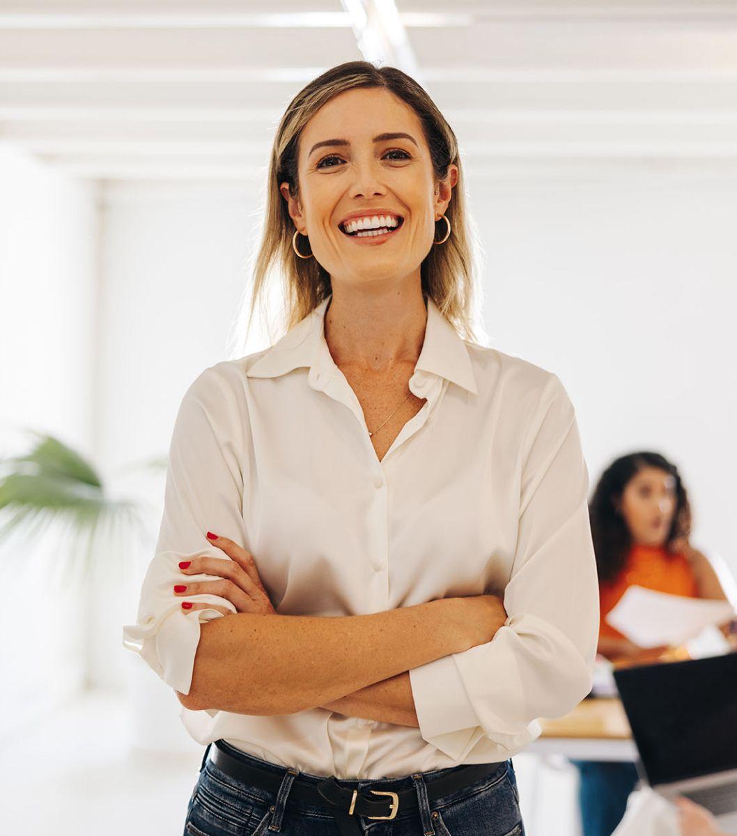 Women with arms crossed wearing a white collared shirt and jeans smiling.