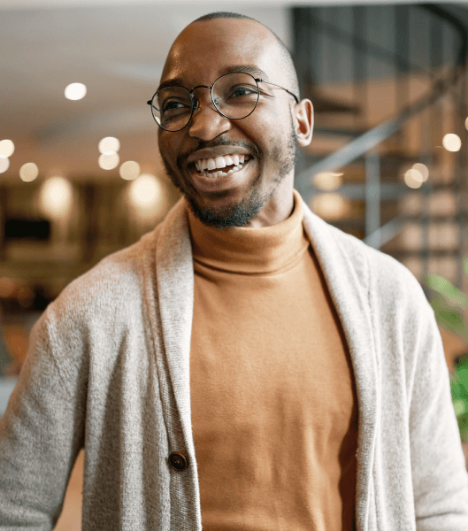 Man wearing light cardigan and burnt orange turtle neck smiling.