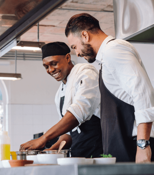 Two men working in commercial kitchen wearing aprons.