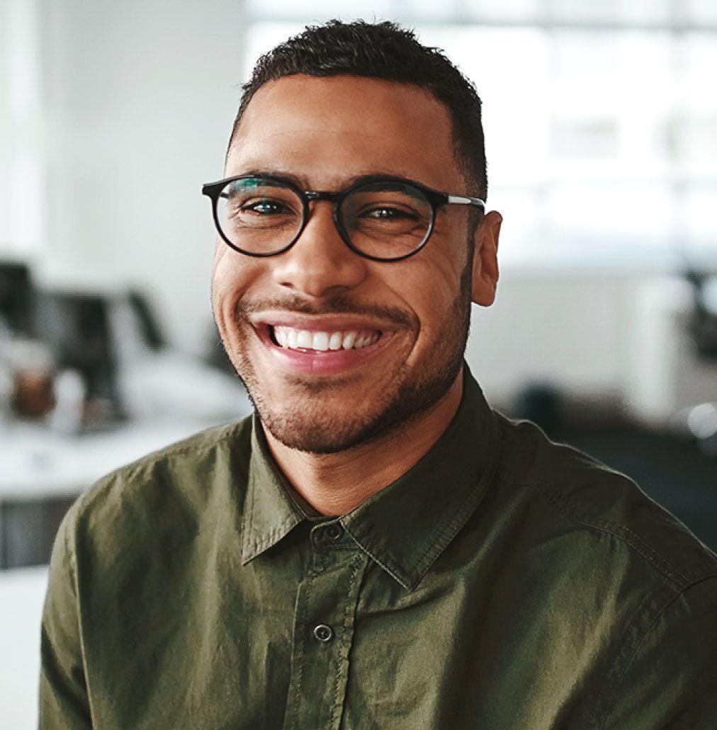 Man with facial hair wearing a green shirt with collar, and glasses smiling and looking into the camera.