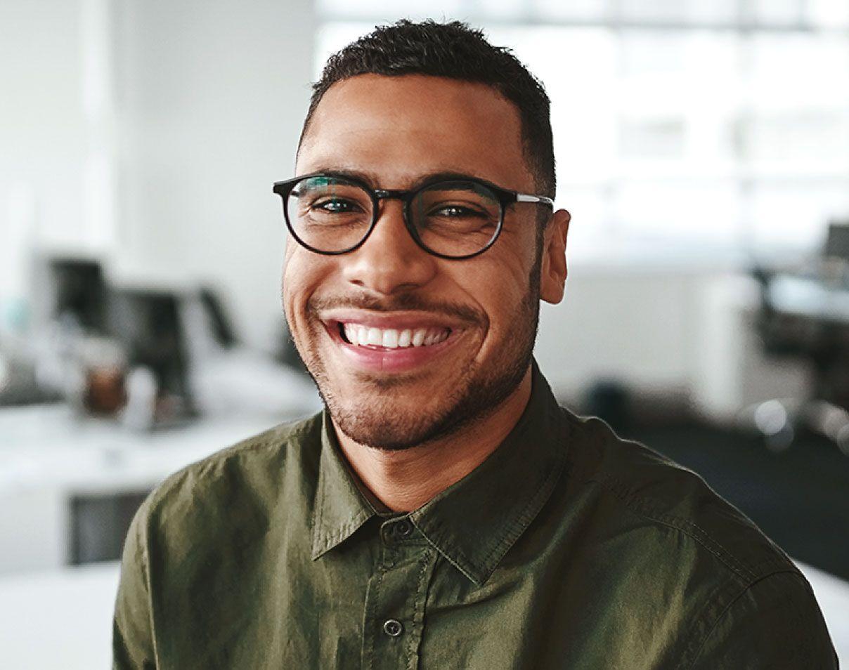 Man with facial hair wearing a green shirt with collar, and glasses smiling and looking into the camera.