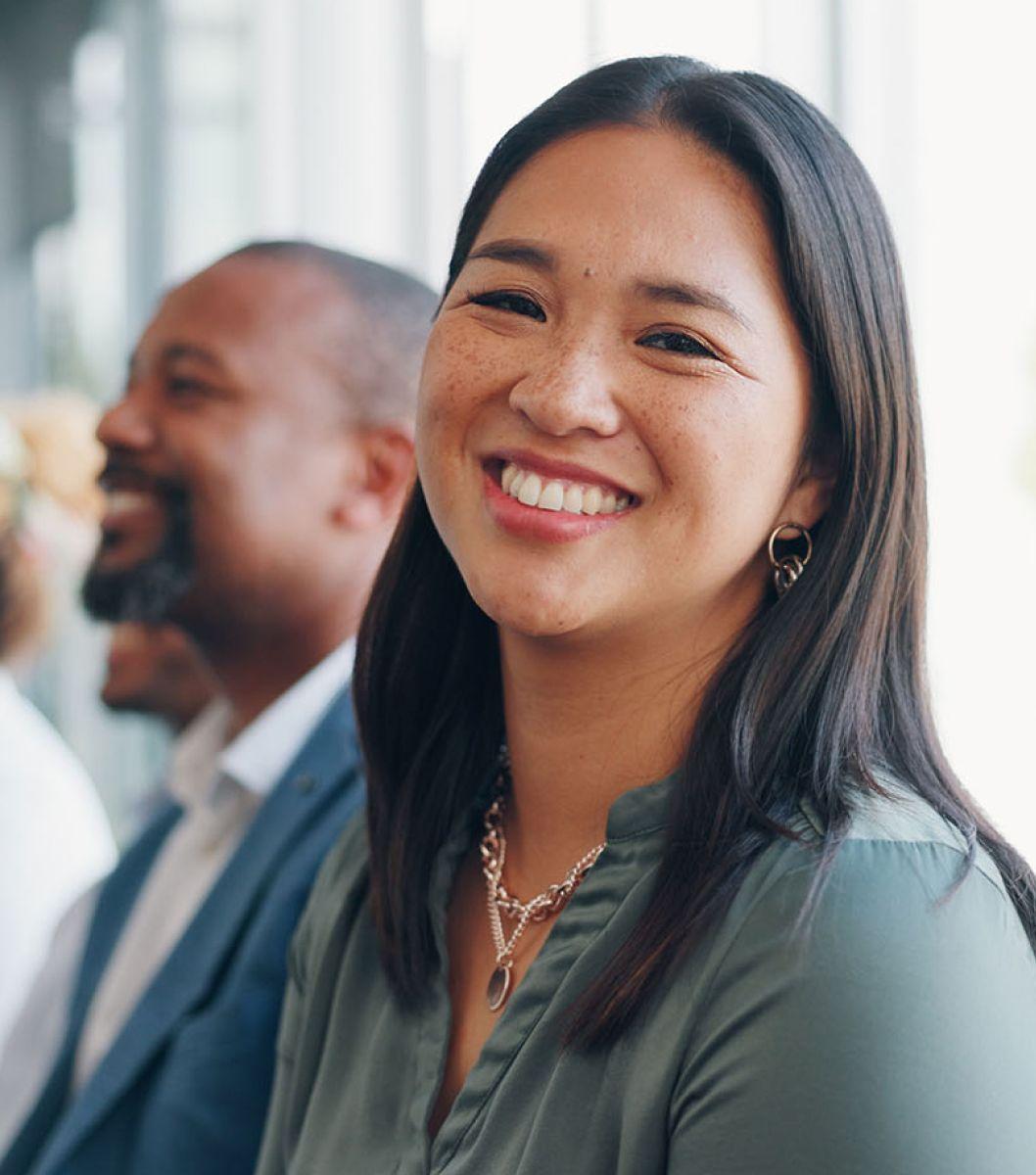 Portrait of women smiling in bright room. A man is seen smiling in the background looking out of frame.